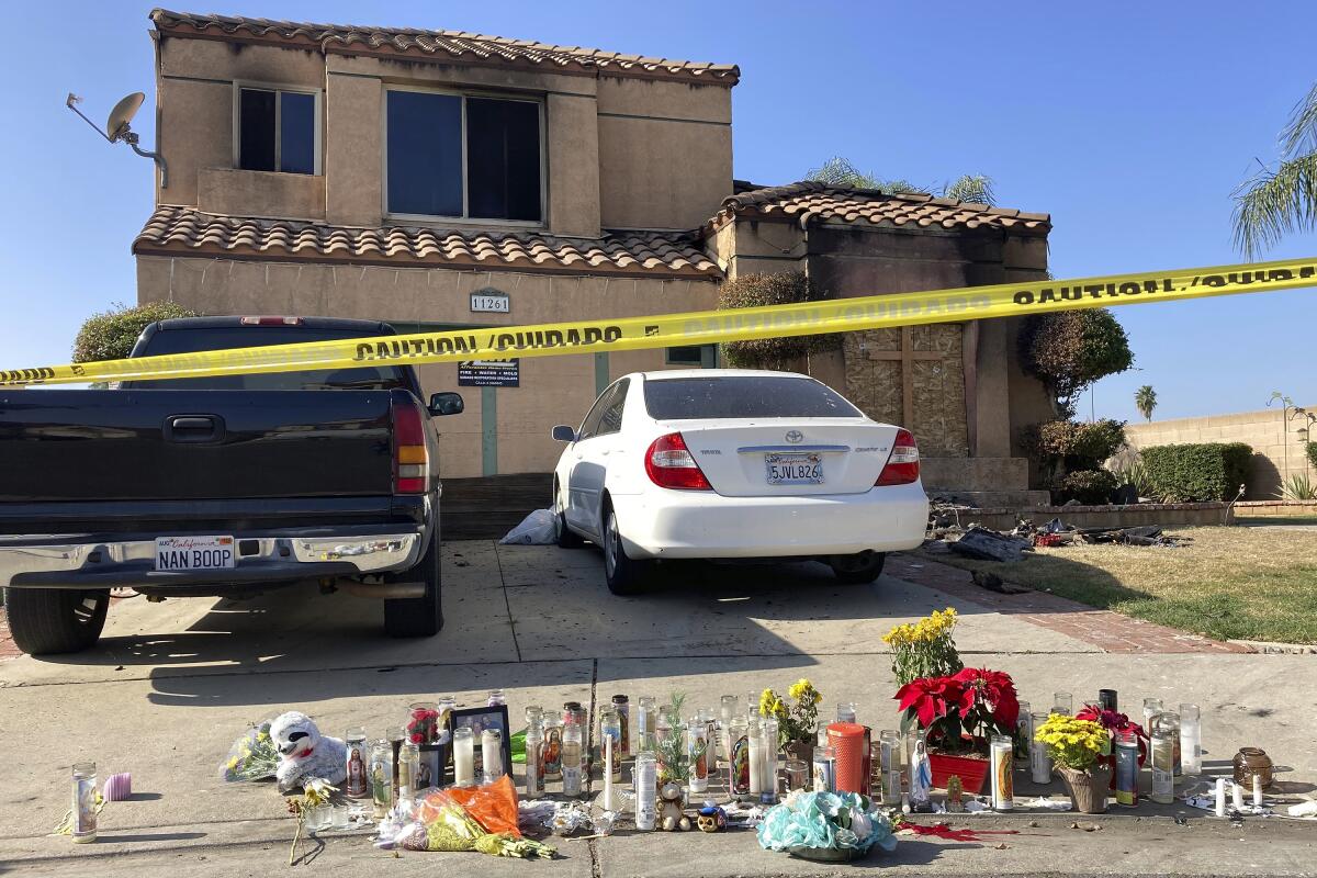 Dozens of candles are laid on the sidewalk, along with bouquets of flowers and stuffed animals outside of a charred home.