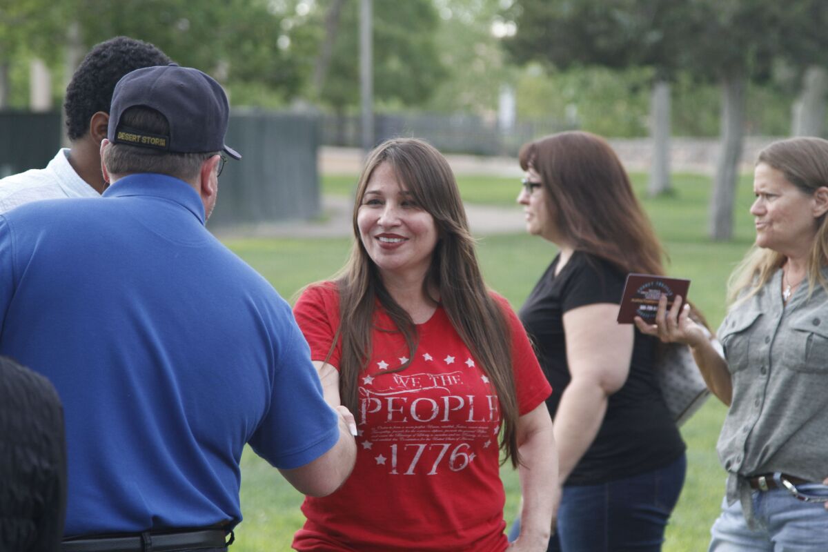 A woman shakes a man's hand in a park as others stand nearby. 