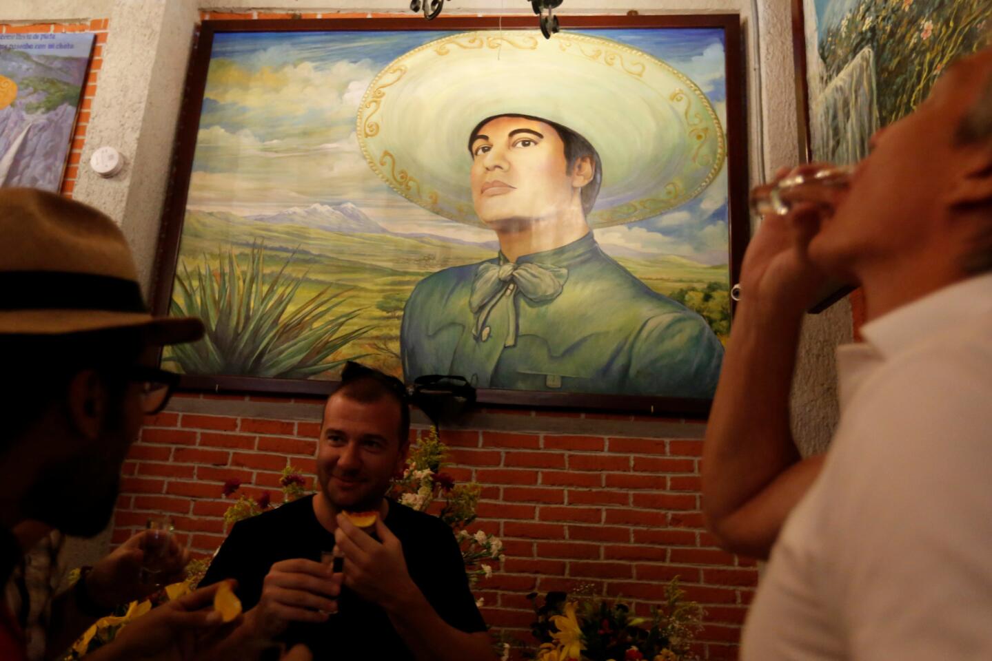Tourist drink tequila next to a painting of iconic Mexican singer and song writer Juan Gabriel after his death, inside a restaurant in Plaza Garibaldi in Mexico City