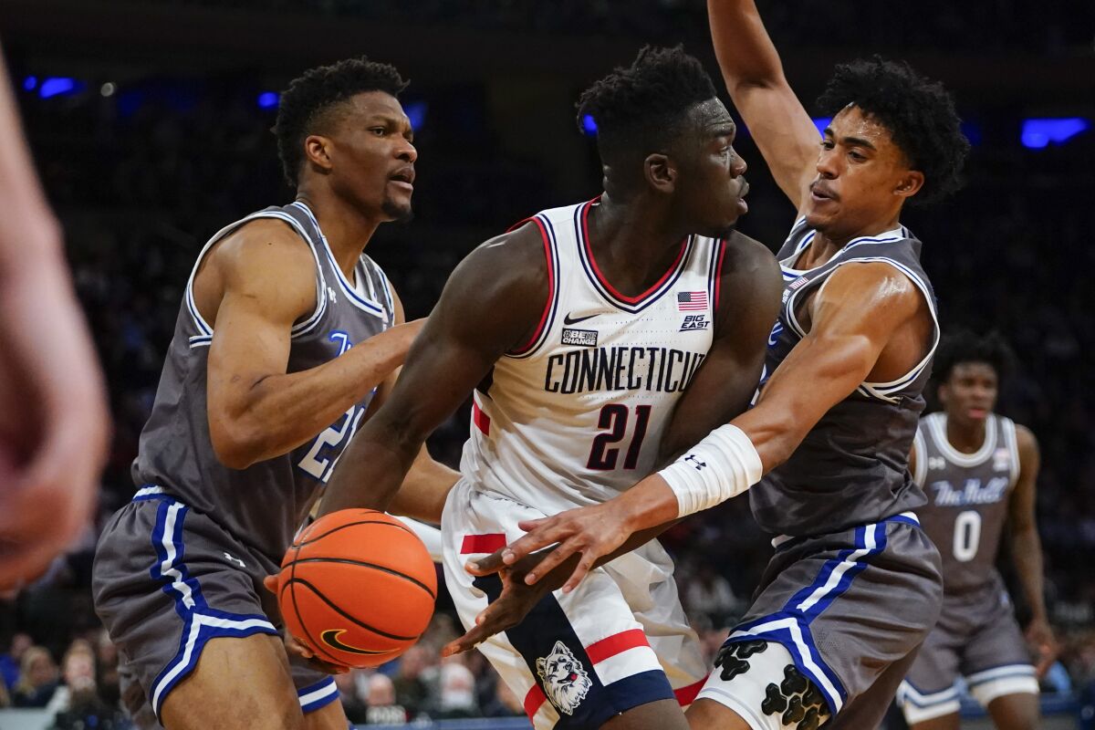 Connecticut's Adama Sanogo (21) passes the ball away from Seton Hall's Ike Obiagu (21) and Jared Rhoden during the first half of an NCAA college basketball game at the Big East conference tournament Thursday, March 10, 2022, in New York. (AP Photo/Frank Franklin II)