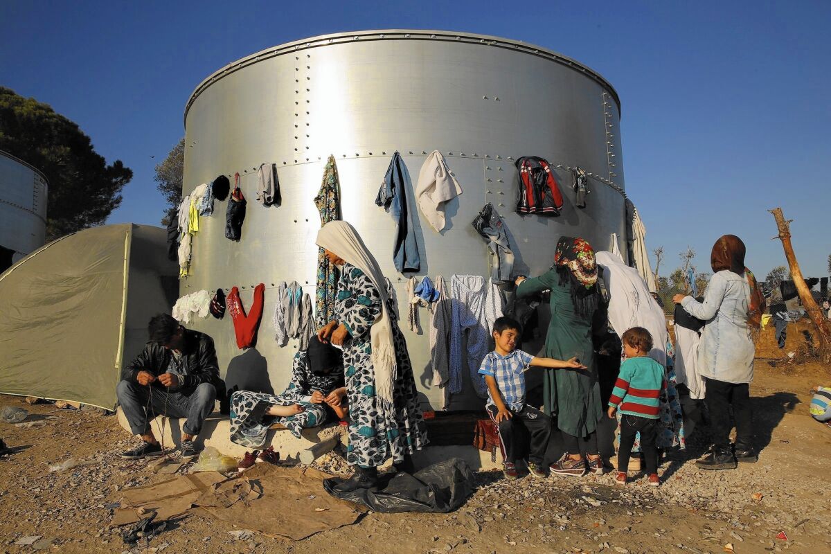 Women hang wet clothes on a steel drum at a refugee camp on Lesbos island, Greece.