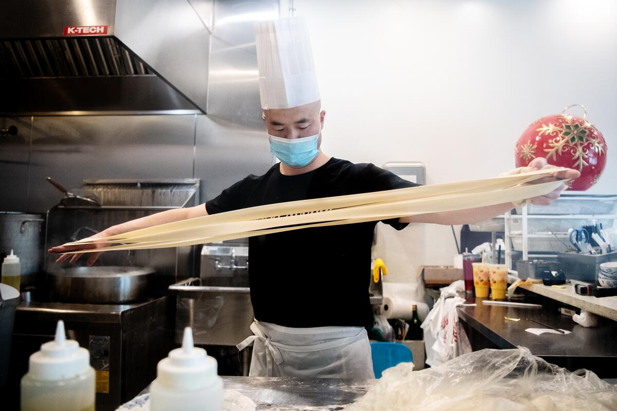 A chef holds his arms wide as he stretches out noodle dough.