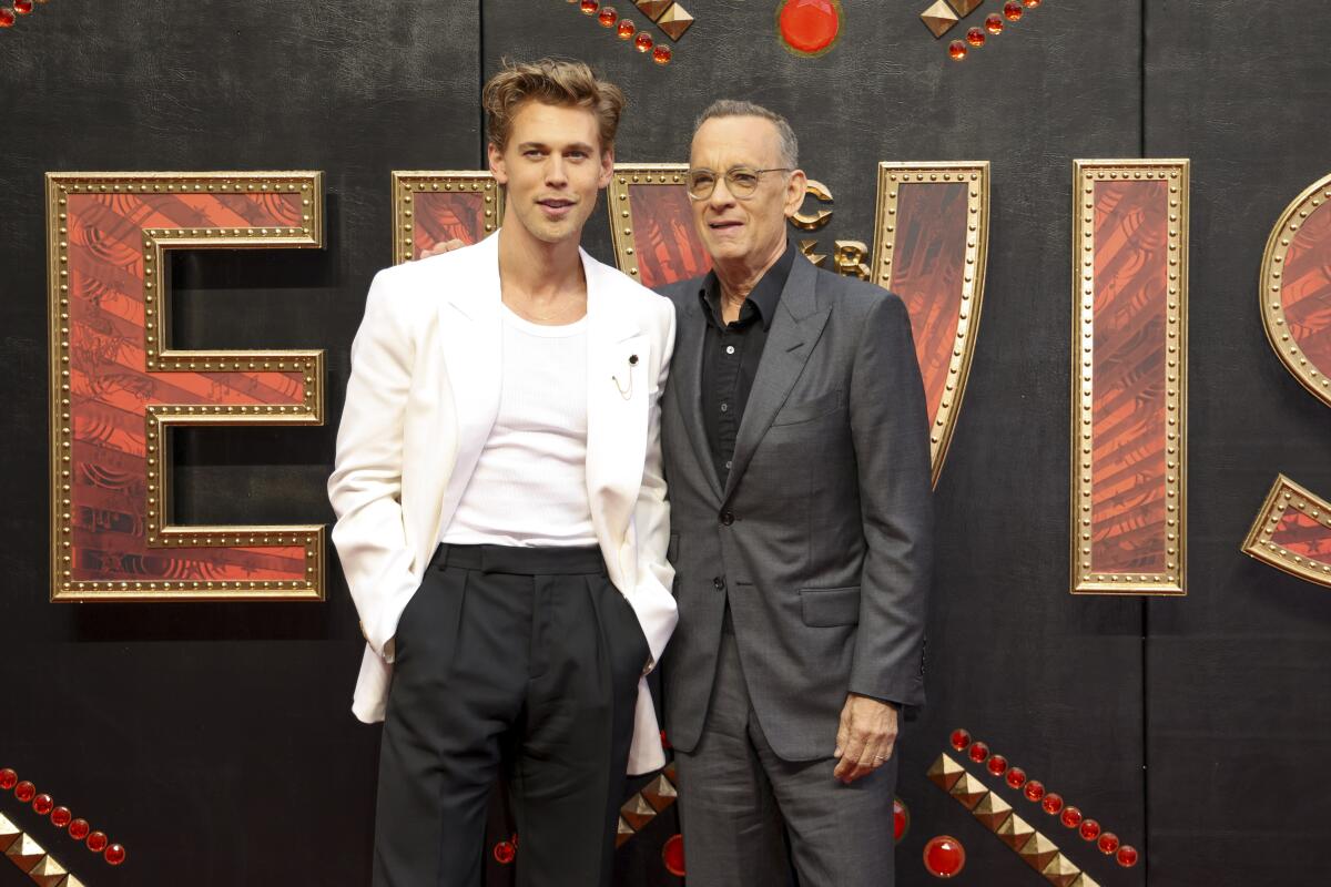 Austin Butler and Tom Hanks pose together in front of a backdrop advertising the film 'Elvis'