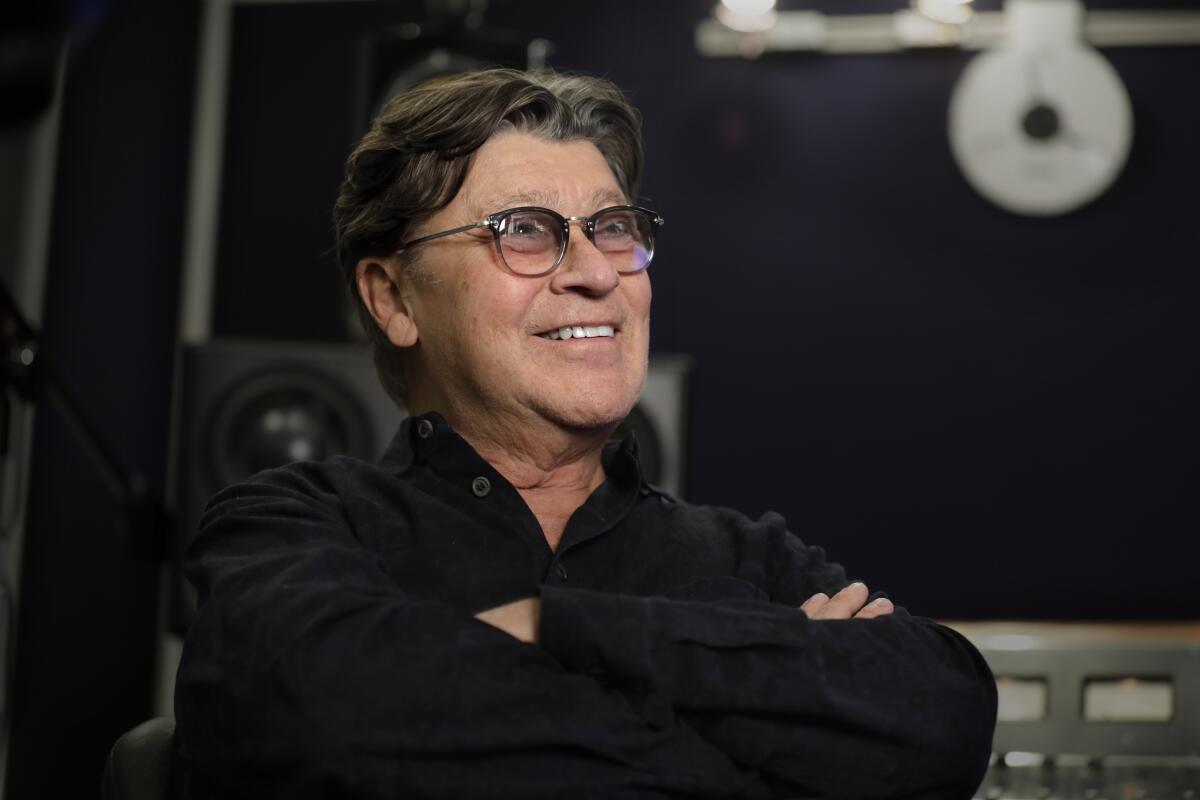 Musician Robbie Robertson crosses his arms and smiles for a portrait.