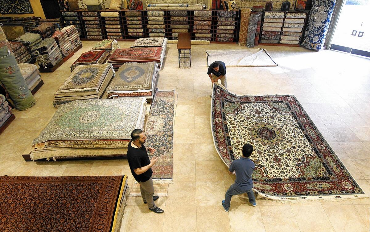 Adel Tousi, left, who runs Tousi Rugs in Westwood, watches as a couple of associates move a carpet. His family has been in the Persian rug industry for five generations, with galleries from Saudi Arabia to California.