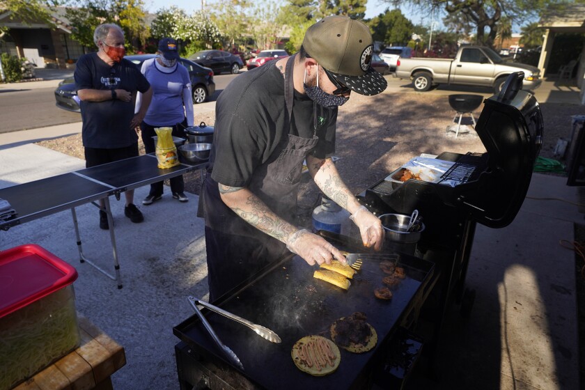 Chef Mike Winneker prepares tacos in front of his home Saturday, April 3, 2021, in Scottsdale, Ariz. Beaten down by the pandemic, many laid-off or idle restaurant workers have pivoted to dishing out food with a taste of home. Some have found their entrepreneurial side, slinging their culinary creations from their own kitchens. (AP Photo/Ross D. Franklin)