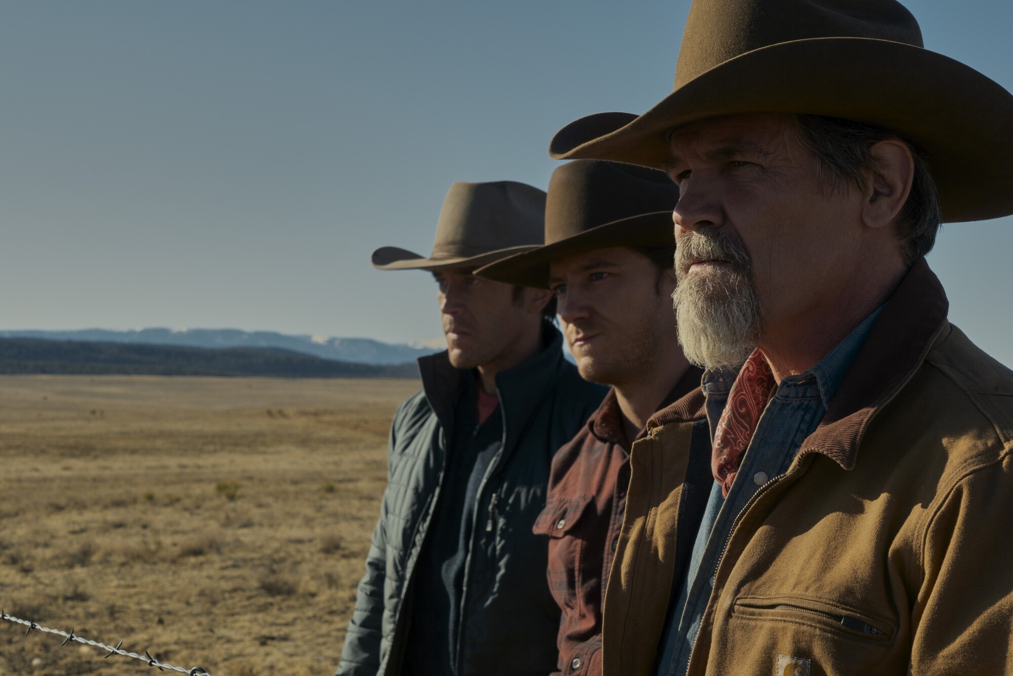 Three men in cowboy hats standing on on the range