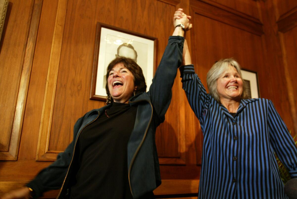 Two women hold each other's hand high and smile in a paneled room