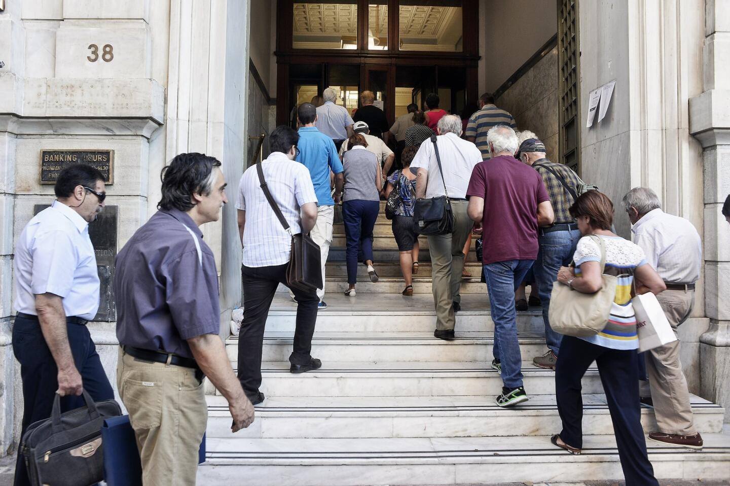 A National Bank official opens the door of a bank branch as people enter after Greek banks reopened on Monday morning after three weeks of closure in Athens.