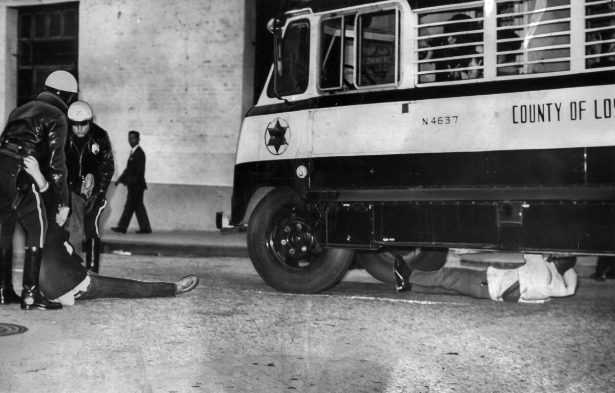 March 10, 1965: As a bus loaded with arrested women prepares to leave the Federal Building in Los Angeles, male demonstrators try to block its departure. The man at left is dragged away from the bus. Marshals then removed the other man from under the bus.