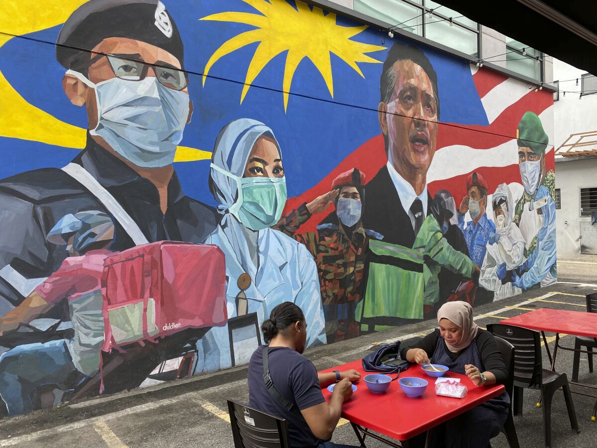 A Malay couple have lunch next to a graffiti tribute to Malaysian workers on the frontlines against the COVID-19 coronavirus at Damansara in Selangor, outside Kuala Lumpur, Malaysia, Saturday, Nov. 7, 2020. Malaysia extended restricted movements in its biggest city Kuala Lumpur, neighboring Selangor state and the administrative capital of Putrajaya from Wednesday in an attempt to curb a sharp rise in coronavirus cases. (AP Photo/Vincent Thian)
