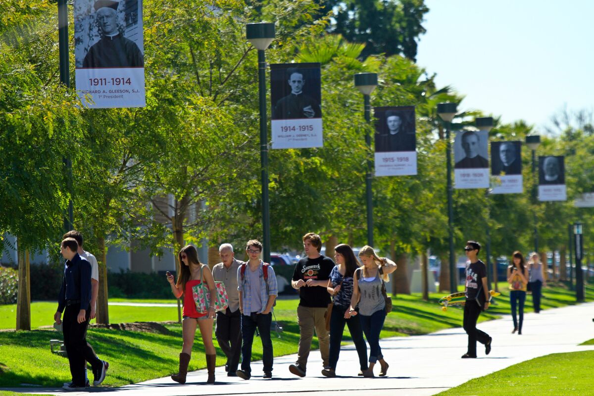 Students walk between classes at Loyola Marymount University under posters of past university presidents.