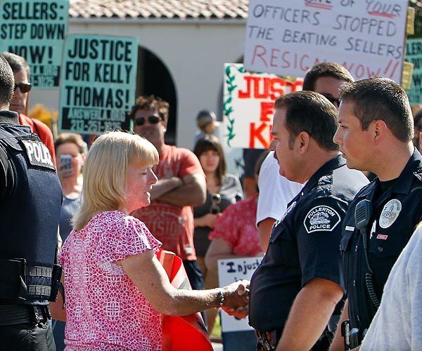 Cathy Thomas, left, shakes hands with Fullerton police officers who barricaded a street to make room for a demonstration protesting the beating and death of Kelly Thomas.