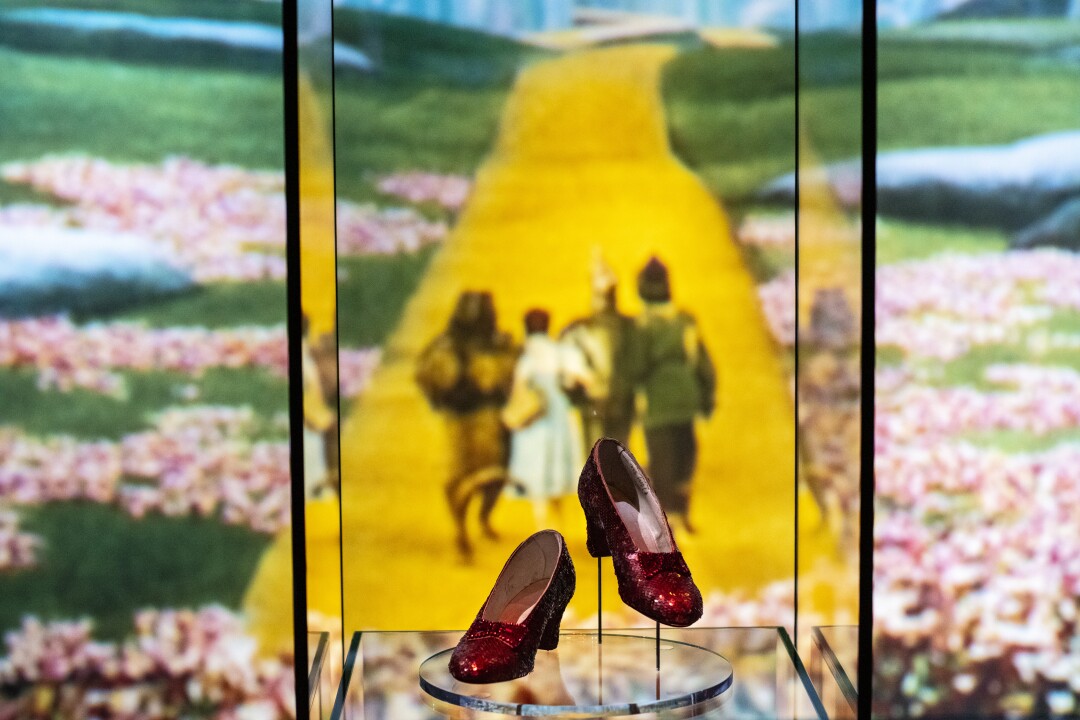 Zapatos de rubí en una vitrina, con la imagen del camino de ladrillos amarillos al fondo