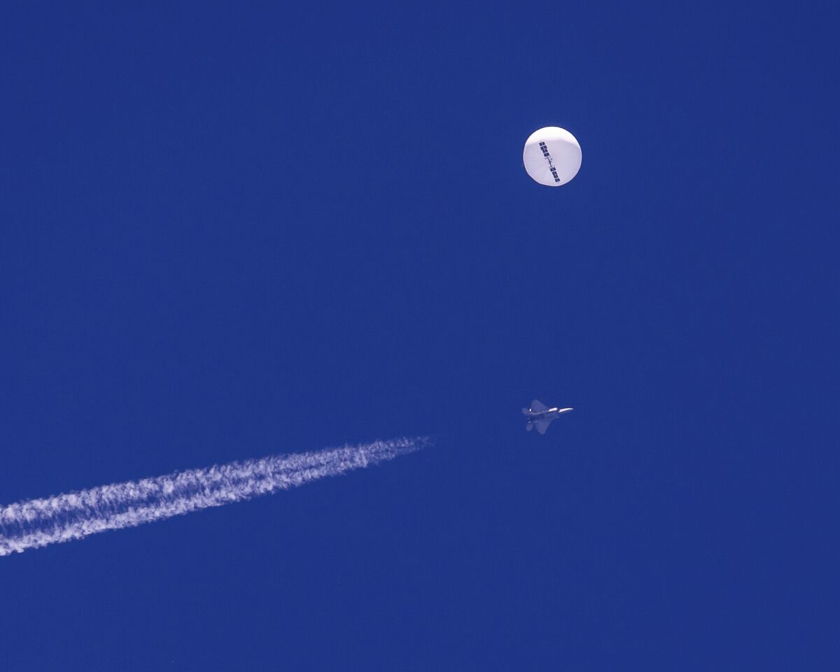 In this photo provided by Chad Fish, a large balloon drifts above the Atlantic Ocean, just off the coast of South Carolina, with a fighter jet and its contrail seen below it, Saturday, Feb. 4, 2023. The balloon was struck by a missile from an F-22 fighter just off Myrtle Beach, fascinating sky-watchers across a populous area known as the Grand Strand for its miles of beaches that draw retirees and vacationers. (Chad Fish via AP)