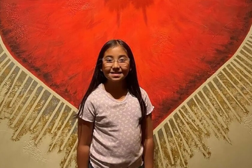 A little girl standing in front of a red and gold mural
