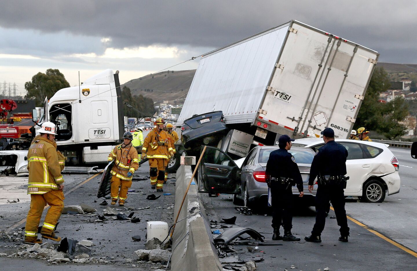 Firefighters and rescue personnel work at the scene after a big rig crashed through the center divider crushing a car underneath and causing four other vehicles to collide on the rain slicked 60 freeway near the Garfield Exit in Monterey Park, Calif.