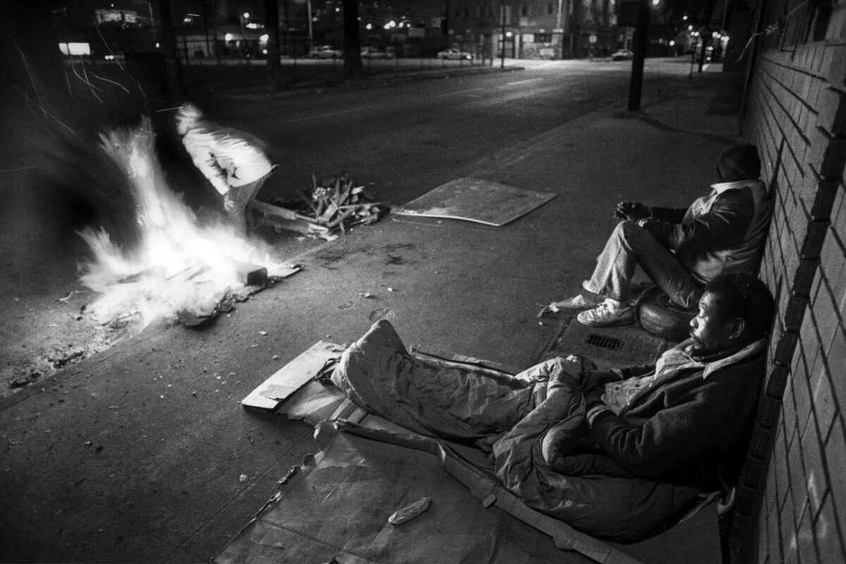 Homeless people warm themselves near an open fire.