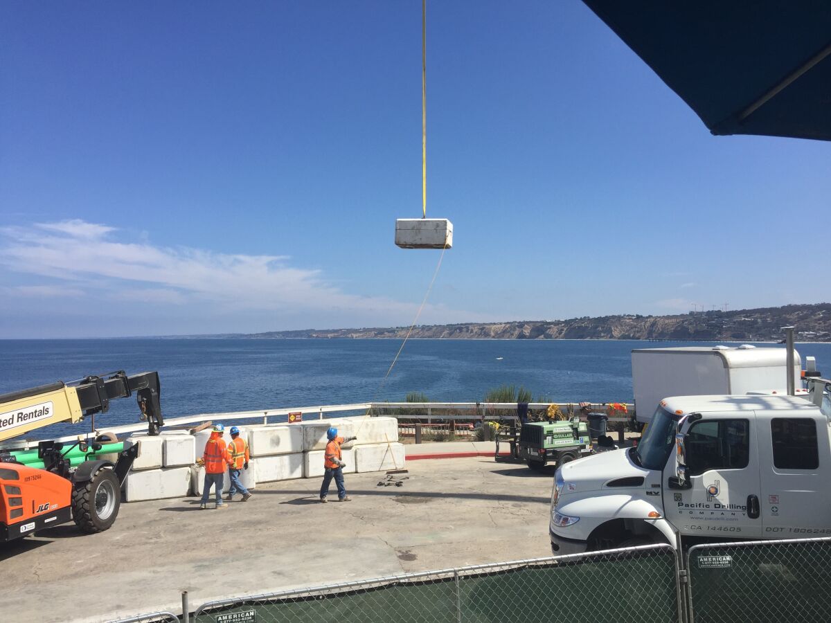 Part of a concrete barrier is lifted by crane over the side of Coast Boulevard to temporarily dam the mouth of the Cook’s Crack Cave, which will then be filled with a slurry.