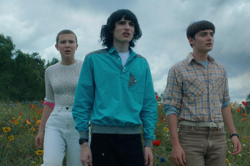 Millie Bobby Brown, Finn Wolfhard and Noah Schnapp walk through a flowery field in their 'Stranger Things' costumes.