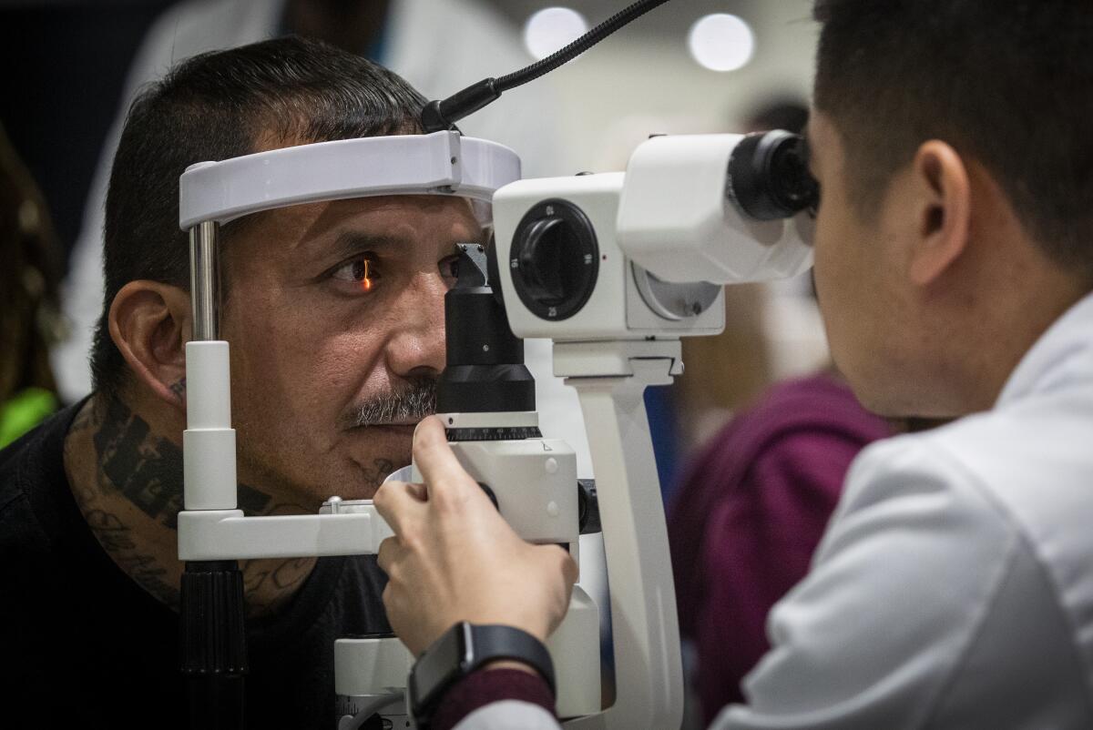 Michael Poblete, right, an optometry student at Western University, performs an ocular health exam in Los Angeles in 2019.