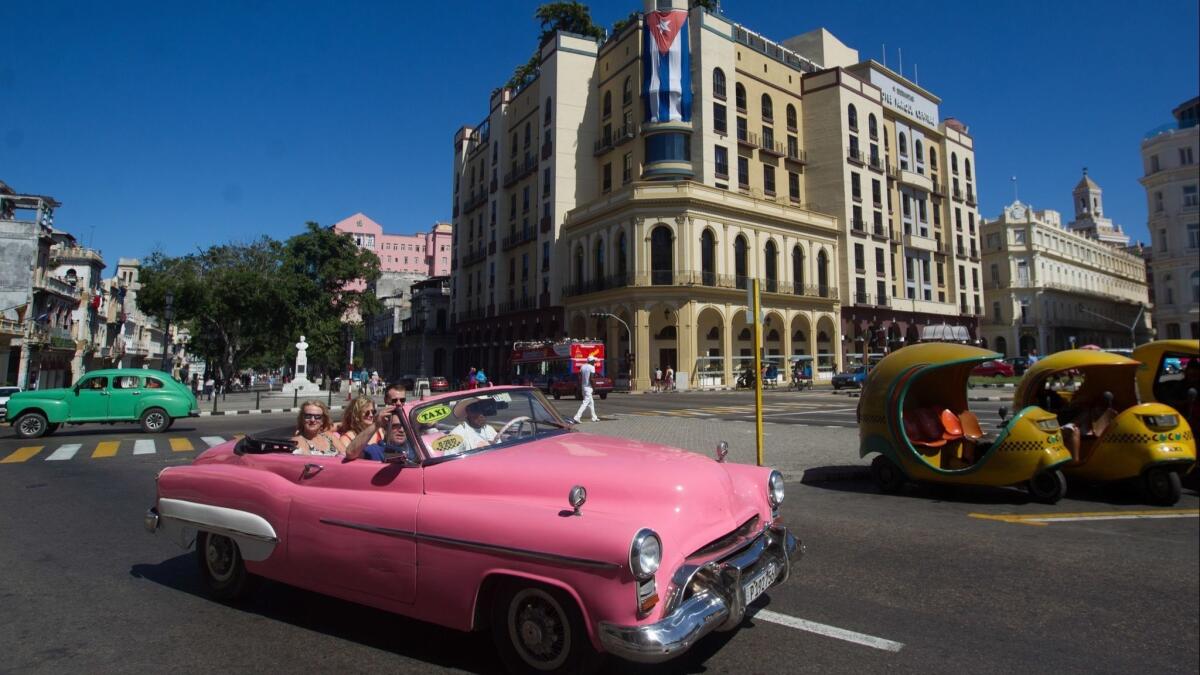 A classic American car travels with tourists through the streets of Havana.