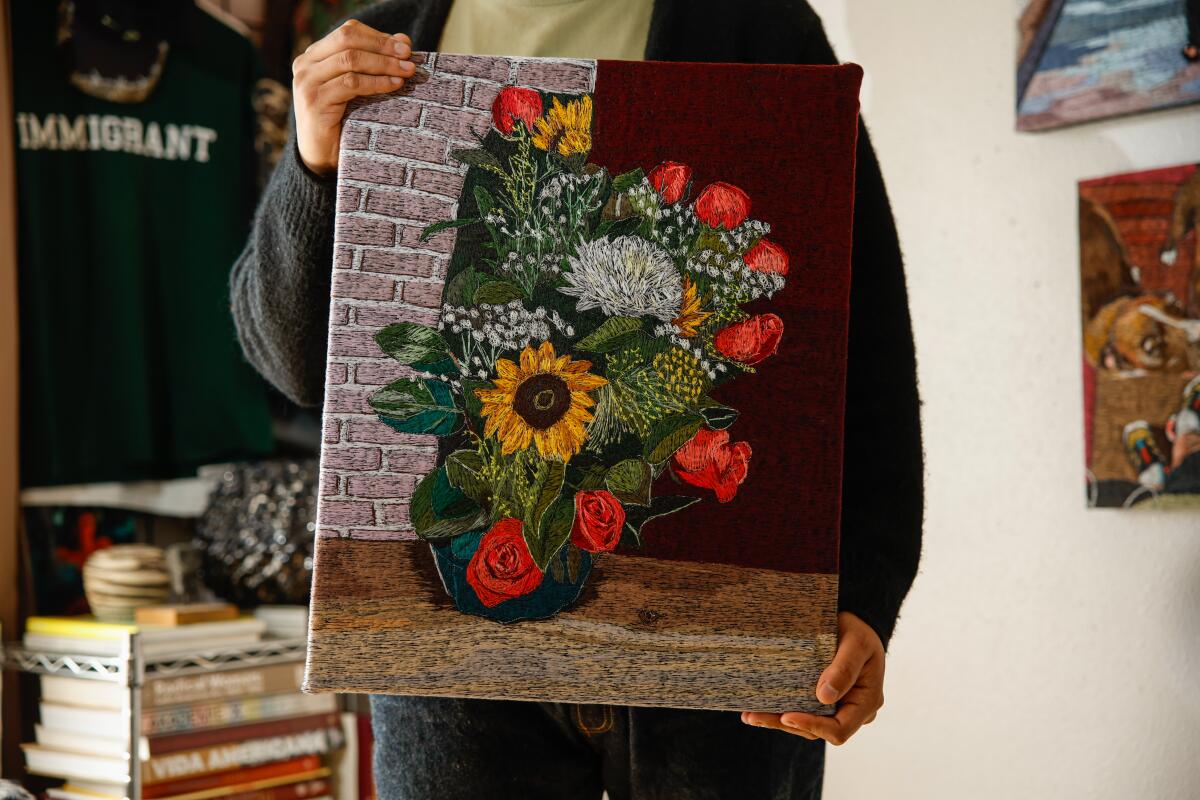 A person holds a textile art piece depicting flowers 