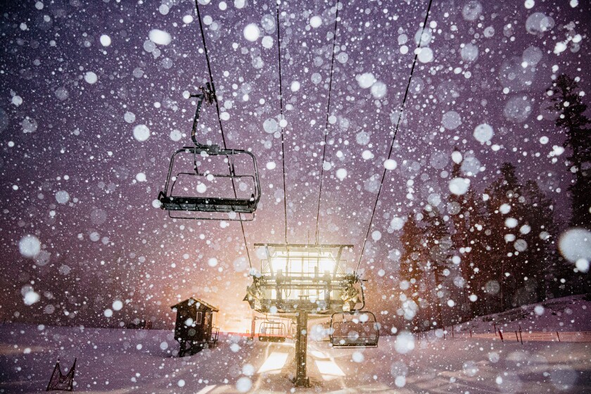 The rising sun highlights snow, and a chair on a ski lift.