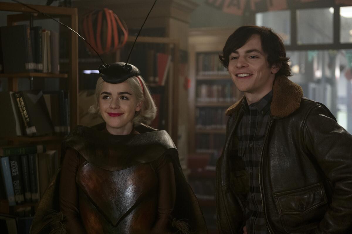 Kiernan Shipka in a bug hat and Ross Lynch smiling in a library