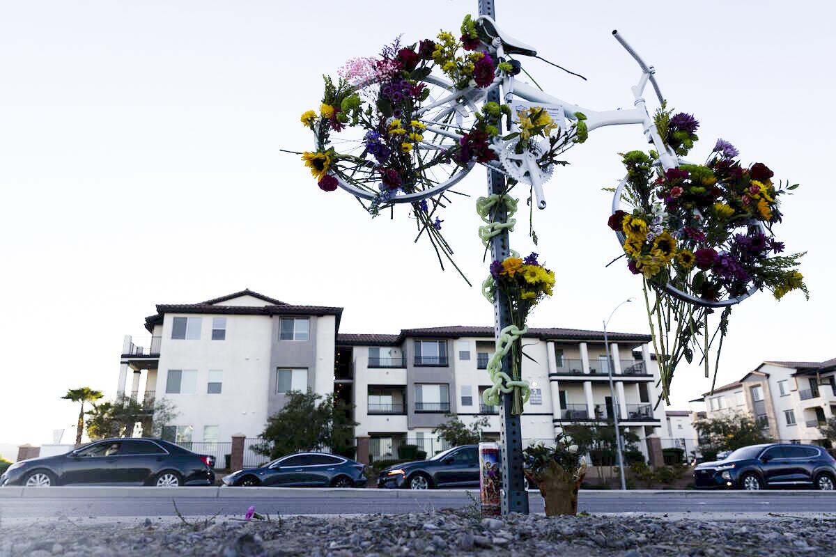 A bicycle covered in flowers hangs from a sign across a residential street from apartment buildings