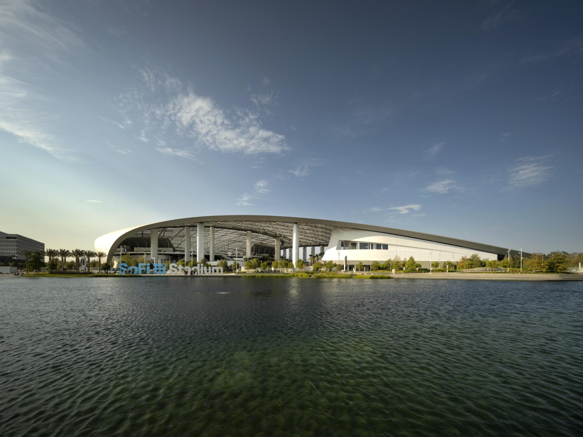 A placid lake sits before a stadium with a curving roofline.