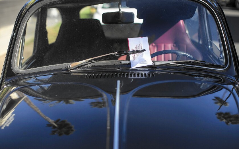 A parking ticket envelope is tucked under the windshield wiper of a car parked in Hollywood on street-sweeping day