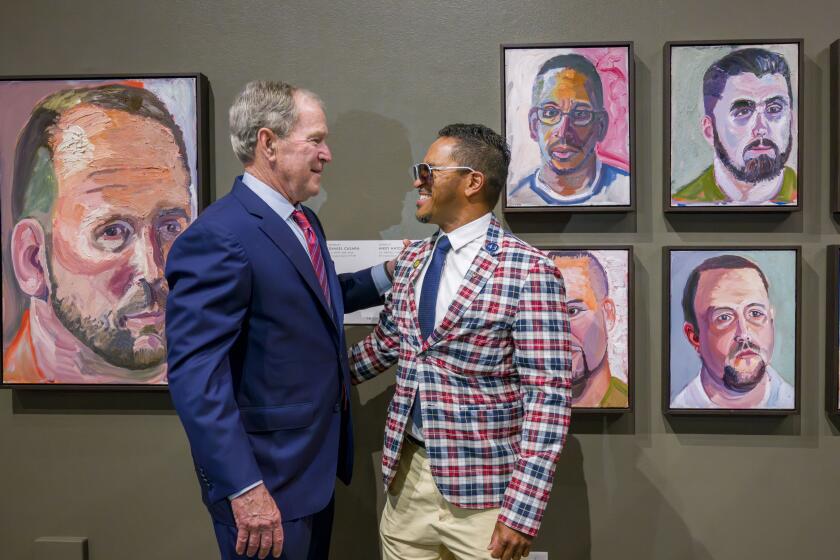 Former President George W. Bush speaks to veteran Daniel Casara of Ramona next to a painting of Casara, top center. 