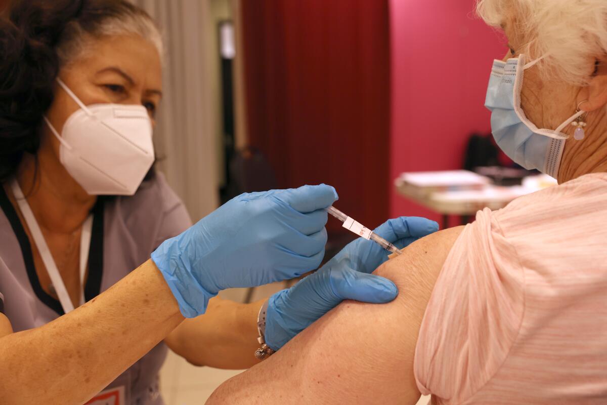 A person in a face mask puts a needle on the upper arm of another person.