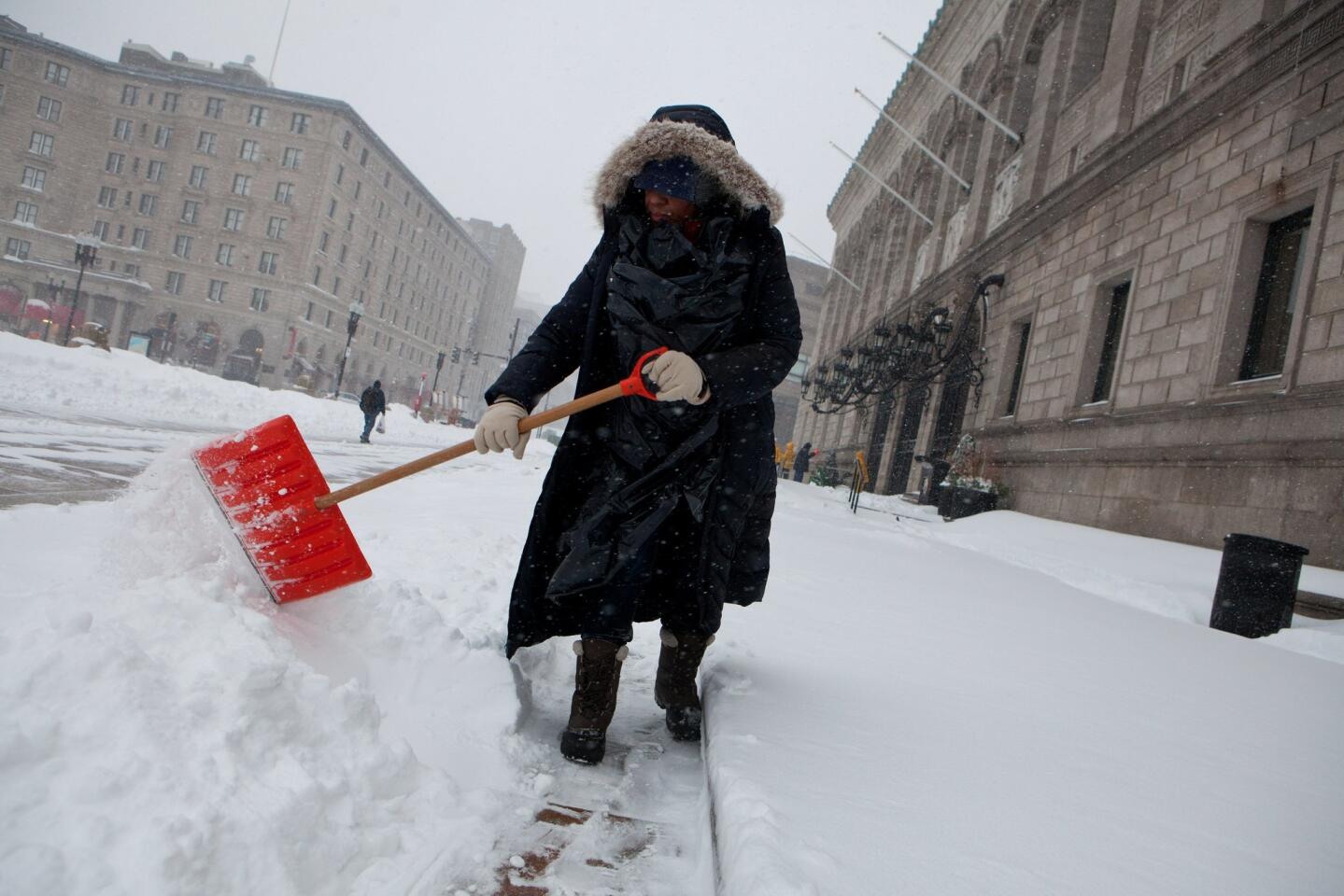 A library employee works to clear the sidewalks in front of the main branch of the Boston Public Library in Boston on Tuesday.