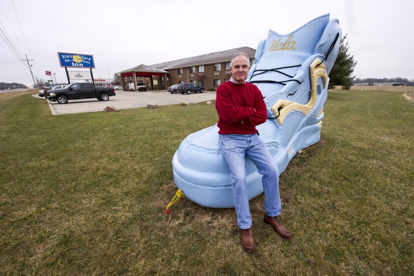 Kenny Cox, owner of the Steve Alford All-American Inn in New Castle, Ind., sits on the big sneaker that has become a local landmark. The shoe is repainted as necessary to represent the current stage of Alford's career.