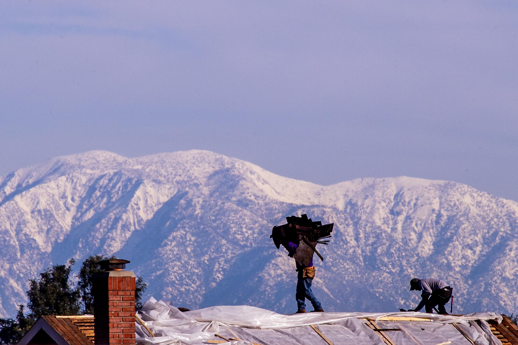 Workers repair a roof covered with plastic sheeing