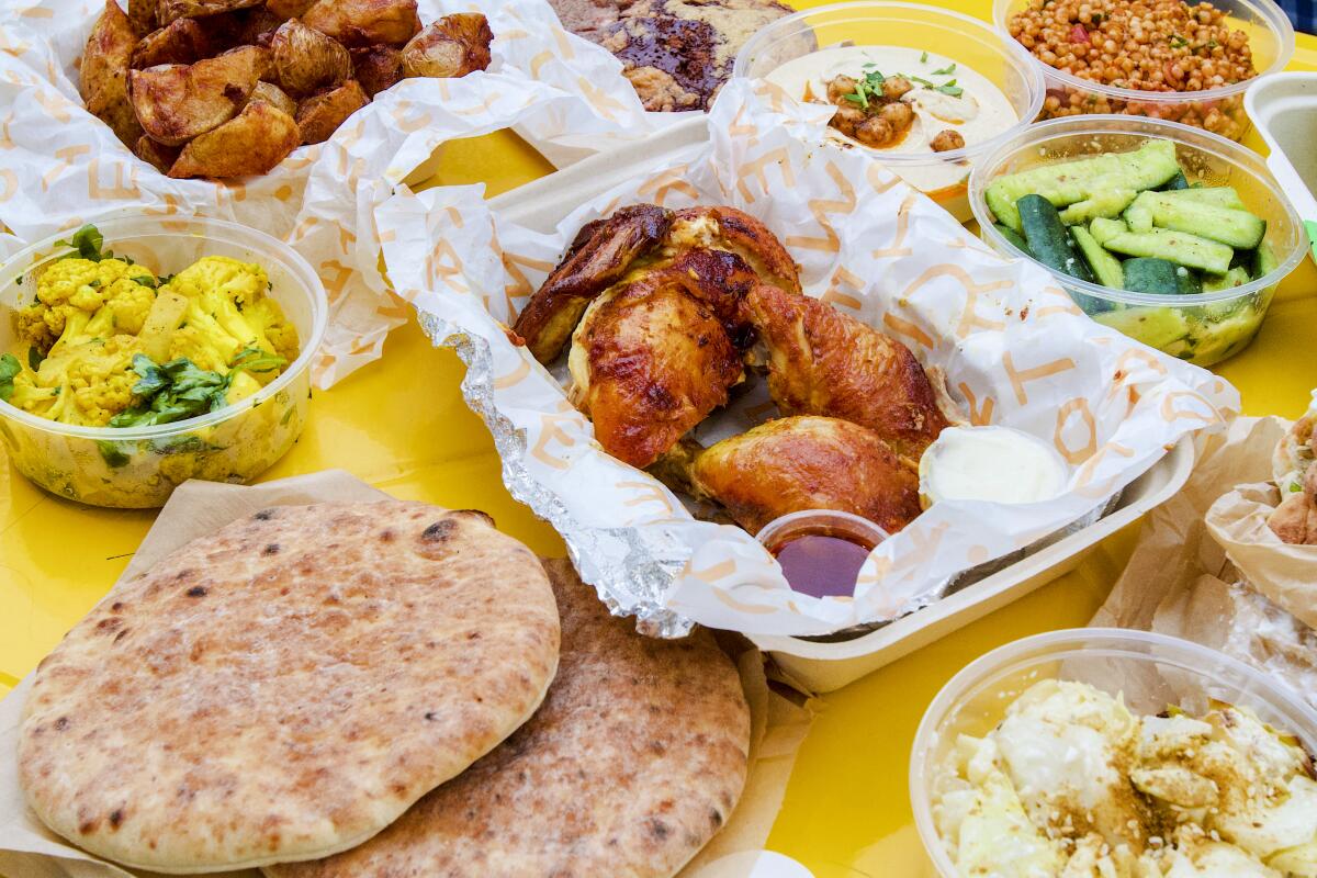 Rotisserie chicken surrounded by vegetable side dishes and pita bread