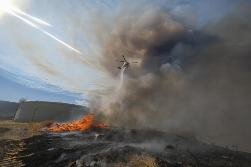 A helicopter drops water at a wildfire in Castaic, Calif. on Wednesday, Aug. 31, 2022. (AP Photo/Ringo H.W. Chiu)