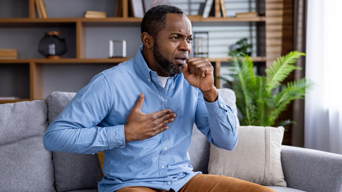 Man at home in distress, clutching chest, coughing may have severe respiratory illness.
