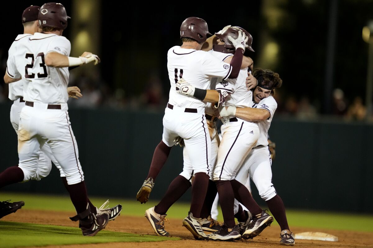 Texas A&M's Troy Claunch, center, is swarmed by teammates after driving in the winning run with a single against Louisville during an NCAA college baseball super regional tournament game early Saturday, June 11, 2022, in College Station, Texas. (AP Photo/Sam Craft)