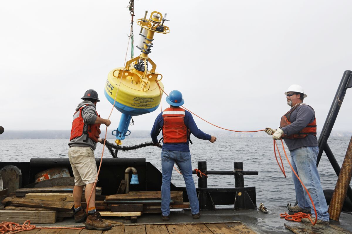 Jeff Pietro, left, and Kris Newhall, center, both of Woods Hole Oceanographic Institution in Massachusetts, help deploy a buoy into the Santa Barbara Channel. Cables connect a listening station on the ocean floor to the buoy, which will transmit audio frequencies to scientists on shore by satellite.