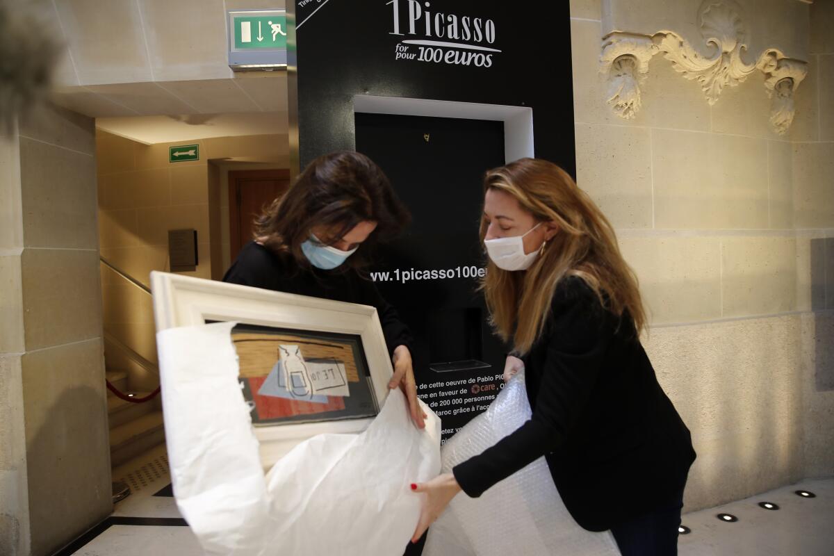 Raffle organizers Peri Cochin, left, and Arabenne Reille unbox the painting "Nature Morte" (Still Life) by Picasso, which was won in the charity draw by an Italian accountant.