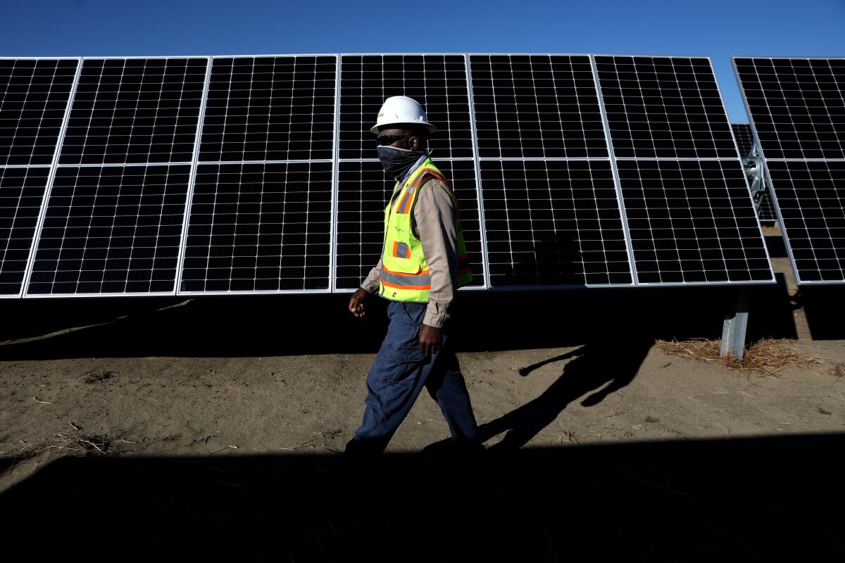 A man in a high-visibility vest walks in front of solar panels