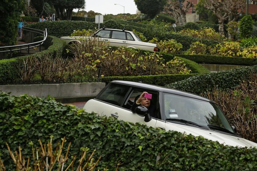 In this Dec. 8, 2015, photo, a woman takes a selfie while riding down the crooked section of Lombard Street in San Francisco. The section of eight hairpin turns, one-way, downhill, starts at Hyde Street. . (AP Photo/Eric Risberg)
