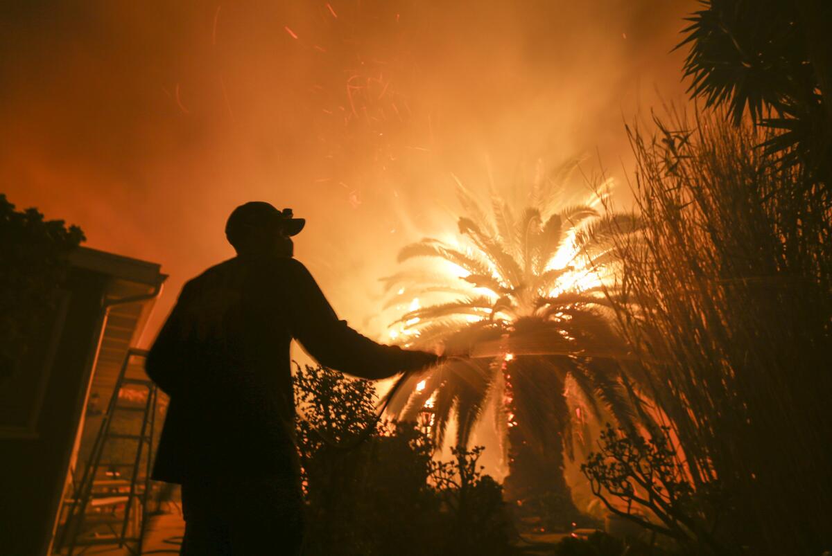 Park Billow, 27, sprays water on the hot spots in his backyard as the Woolsey fire burns in Malibu.