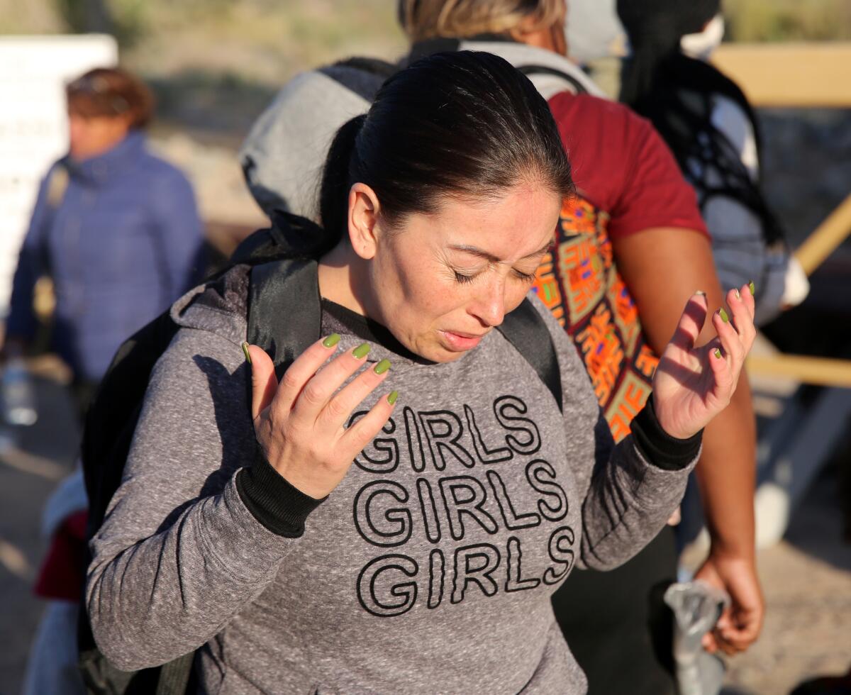 A woman lifting her hands and bowing her head as she stands near others in the sunlight