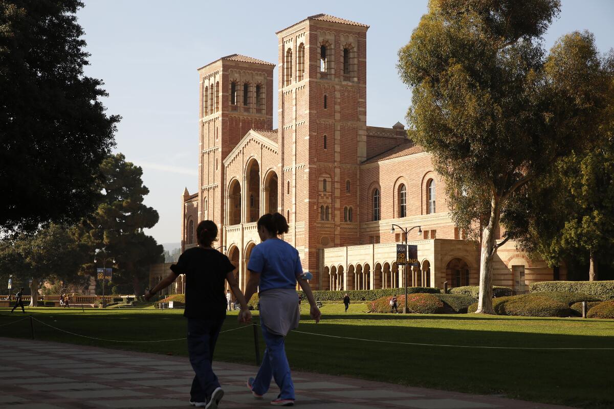 Two people hold hands as they walk past a building with two towers flanking its entryway.
