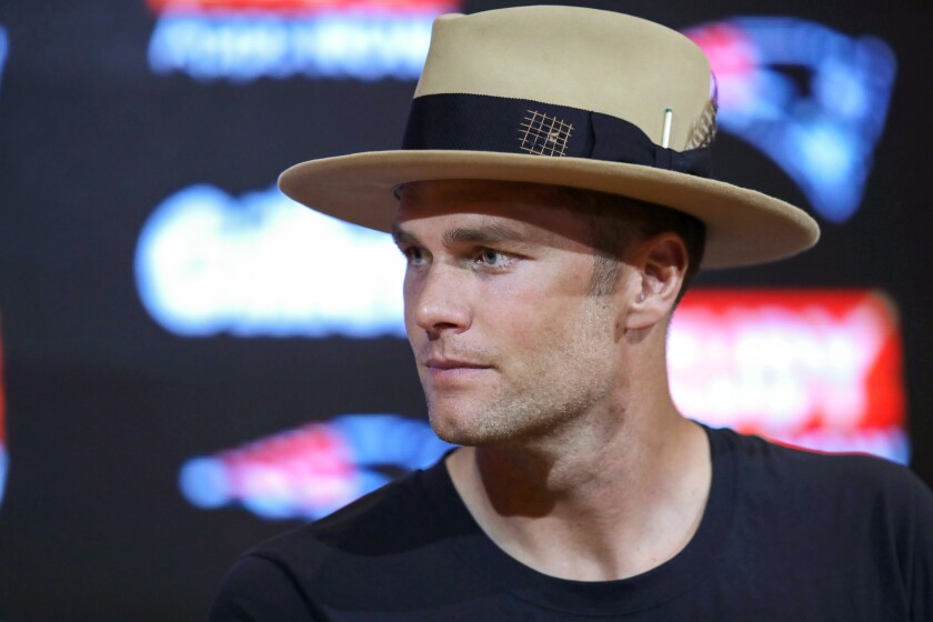 Tom Brady speaks to the media while wearing a hat.