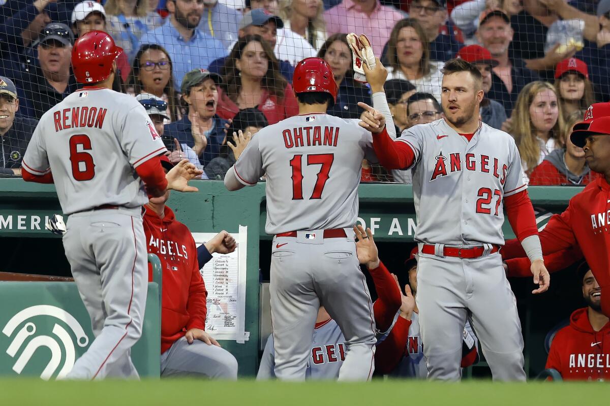 The Angels' Anthony Rendon and Shohei Ohtani are greeted in the dugout by Mike Trout after scoring on a first-inning double.
